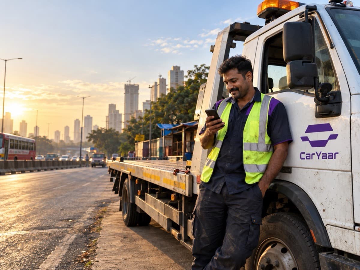 A CarYaar flatbed at first light on a Mumbai road, the driver checking the job on his phone