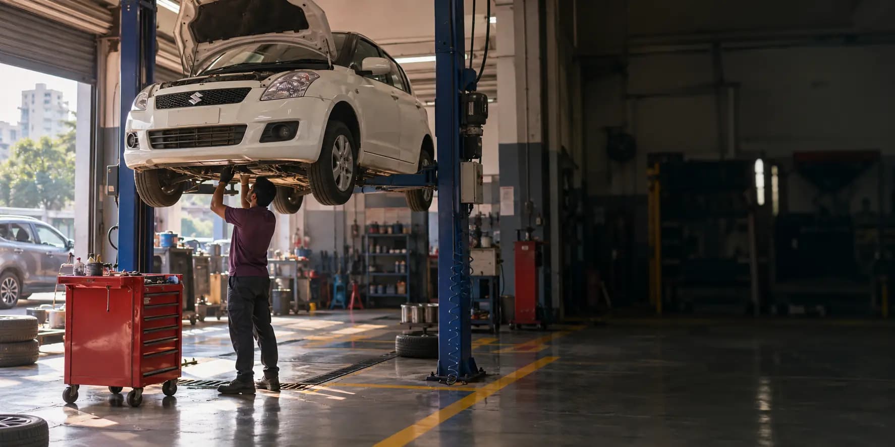 A CarYaar technician in a purple polo working underneath a white Maruti Swift raised on a blue two-post lift, in a CarYaar Service Partner workshop.