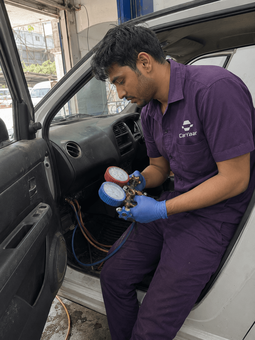 CarYaar technician in the driver seat using a twin-dial AC manifold gauge to check refrigerant pressure.