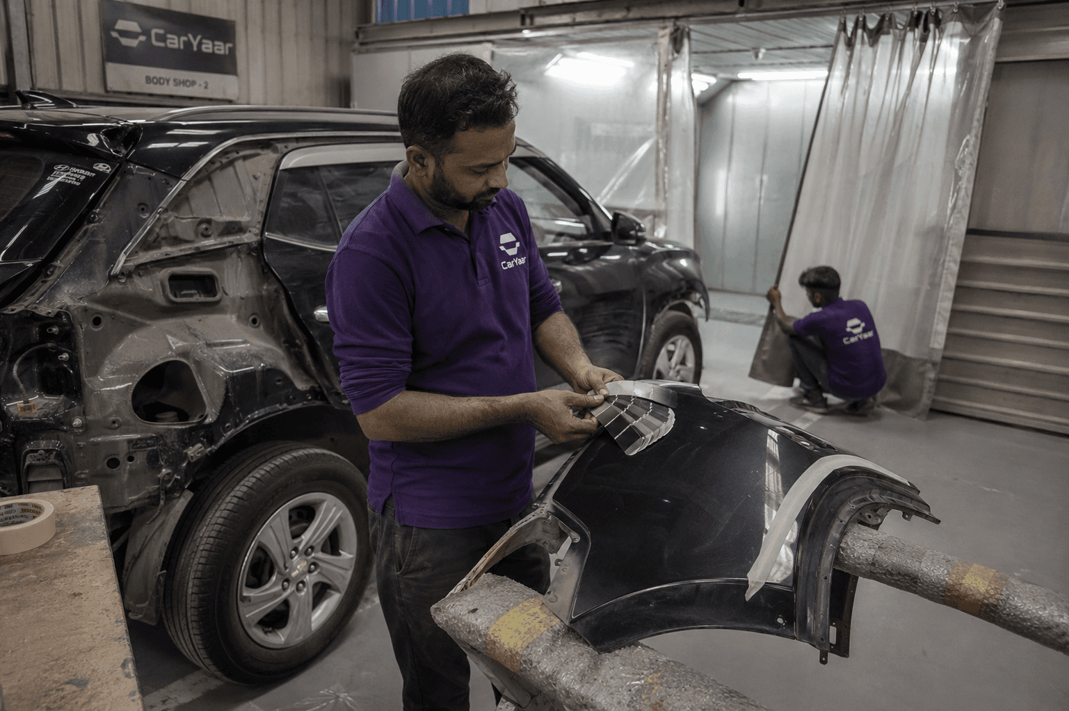 CarYaar body shop technician inspecting a removed body panel inside the workshop.
