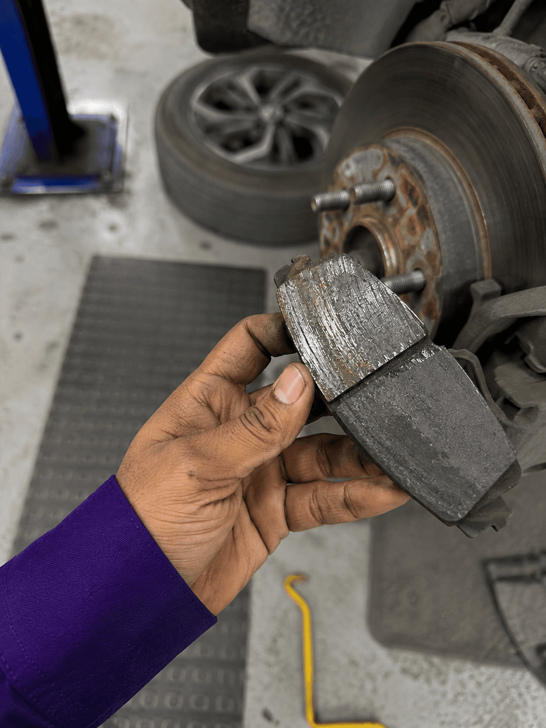 CarYaar technician holding up a worn brake pad next to the brake disc of a lifted car.