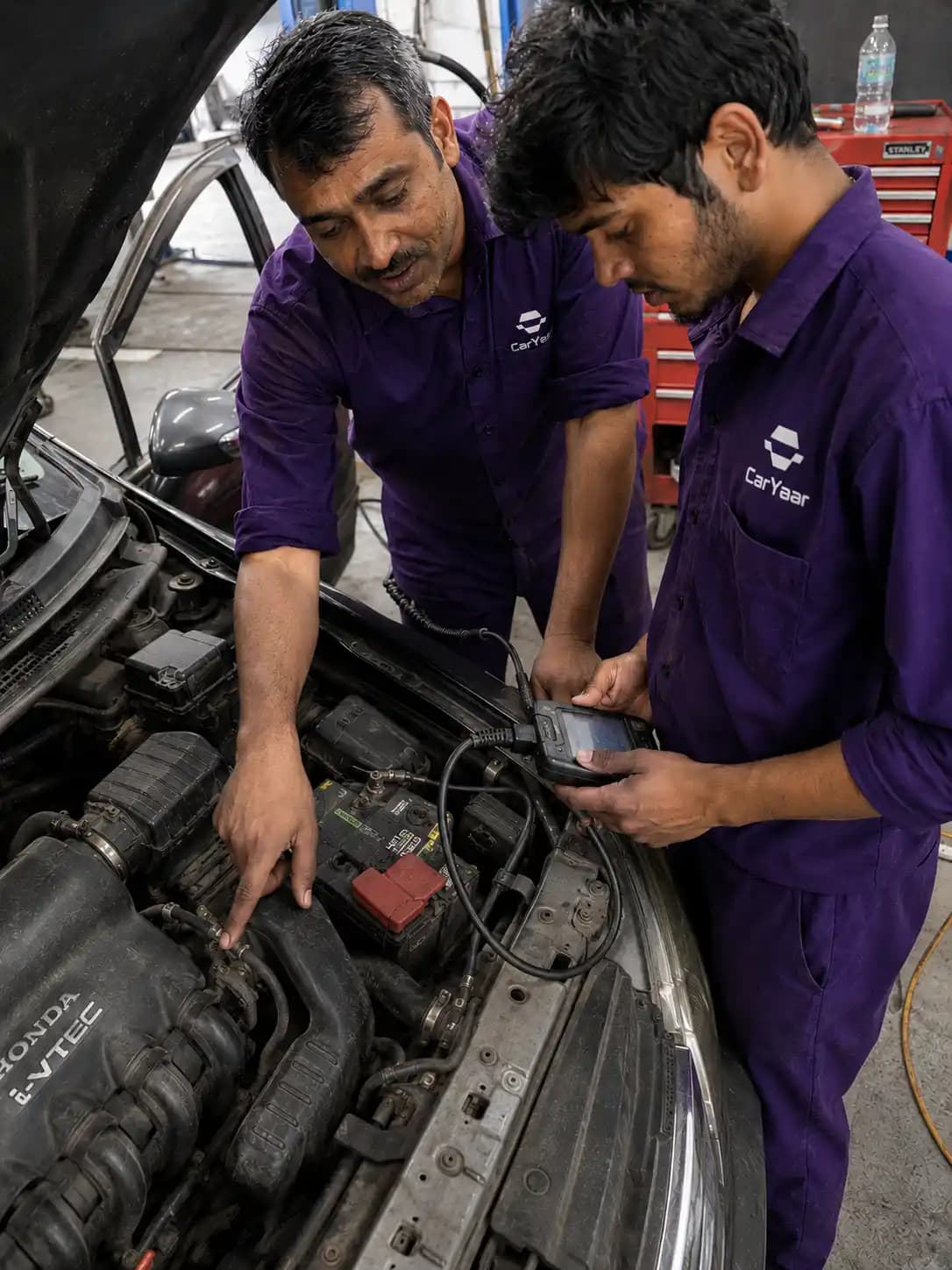 Two CarYaar technicians running a diagnostic scanner on an open engine bay, doing only the items the customer approved.