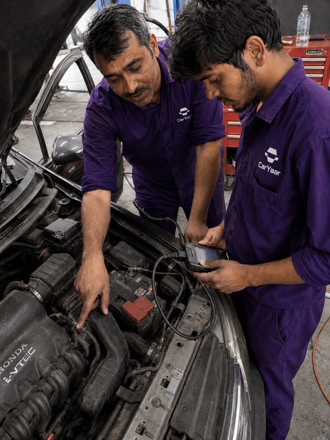 Two CarYaar technicians inspecting an open engine bay with a handheld diagnostic scanner.