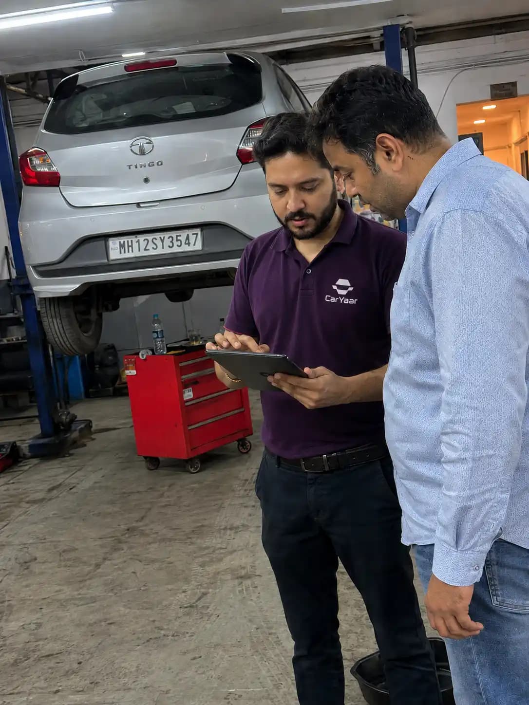 CarYaar service advisor walking a customer through the fixed plan price on a tablet, the car up on the lift behind them.