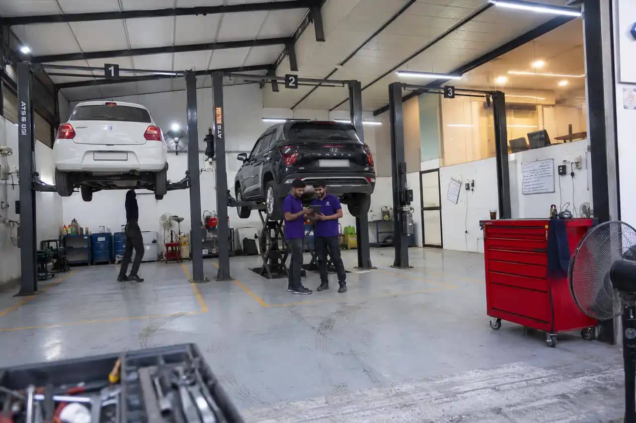 A three-bay CarYaar Service Partner workshop, two cars up on the lifts and two technicians checking a job on a tablet.