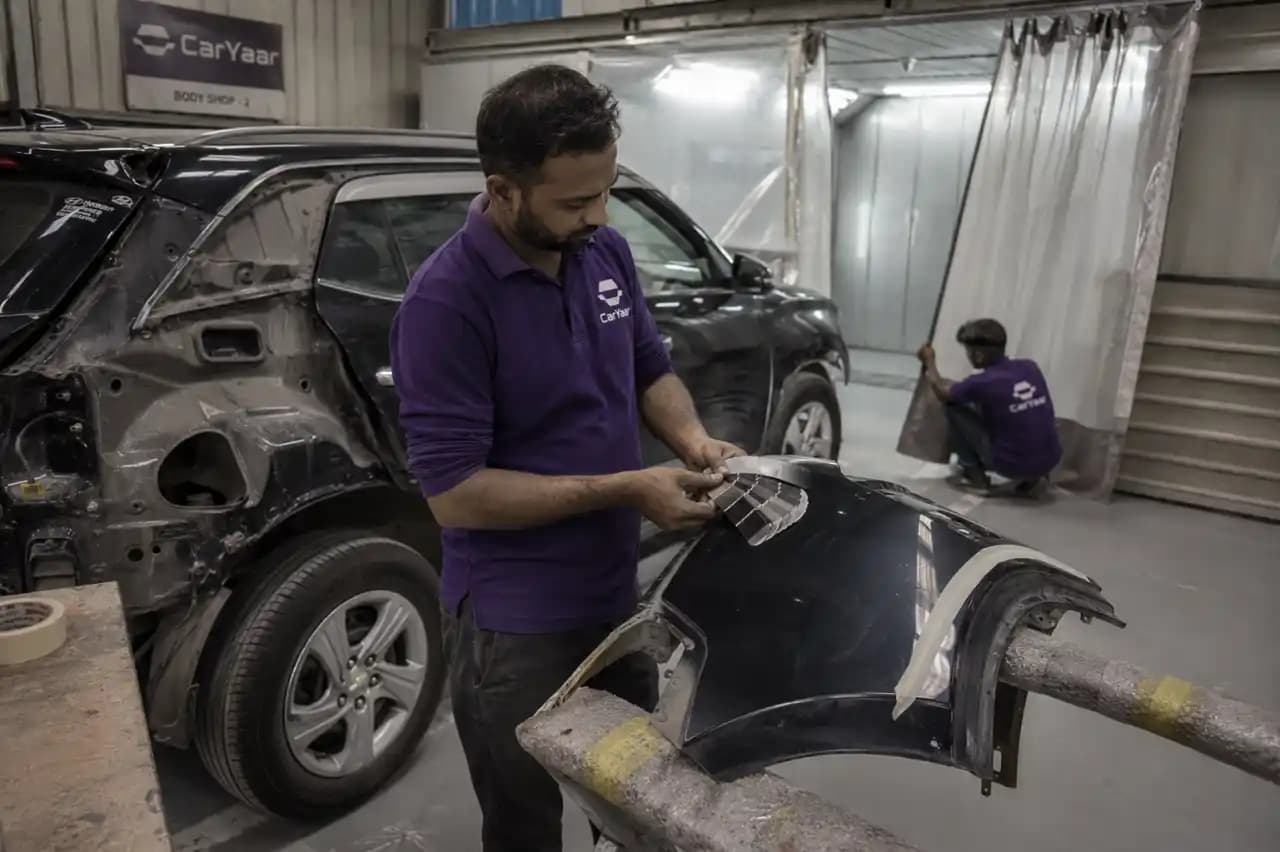 CarYaar body shop technician inspecting a removed body panel inside the workshop.